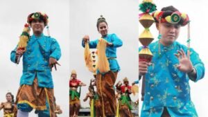 Penari Tari Ganjur dengan kostum biru keemasan khas Kutai, membawa properti kipas dan gada.